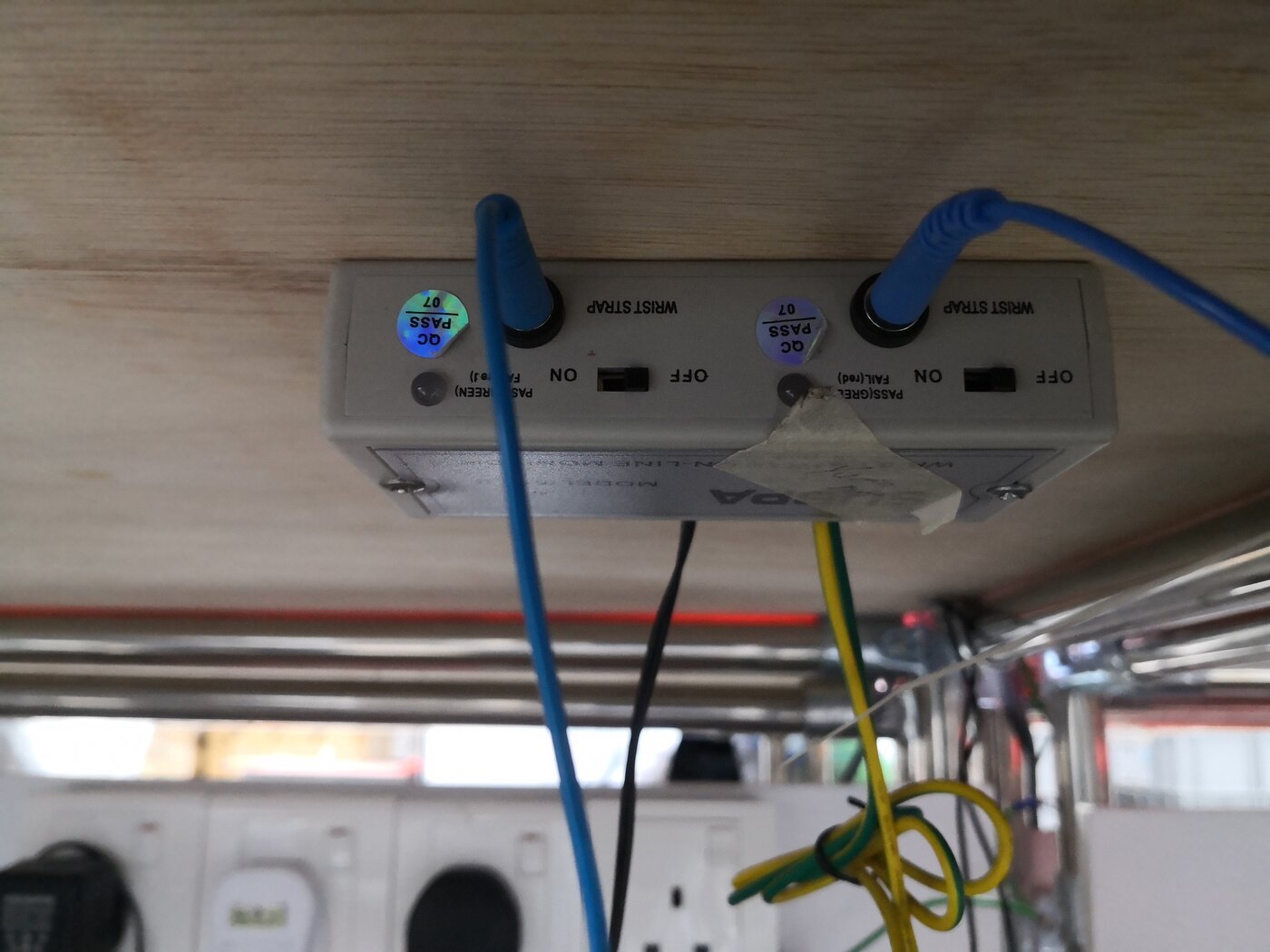 Monitor contínuo de pulseira antiestática instalado sob uma bancada, com dois cabos ligados e fio de aterramento verde e amarelo