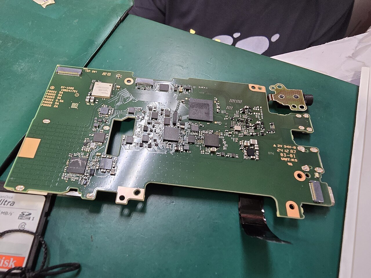 Placa principal de uma câmera fotográfica sobre manta verde de bancada, já limpa após reparo de dano por água