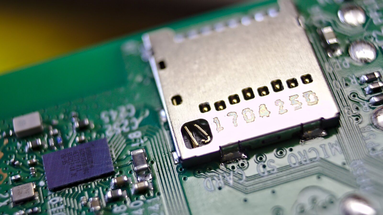 Macrofotografia do conector de cartão microSD soldado na placa de um Raspberry Pi 3, com trilhas e componentes SMD ao redor